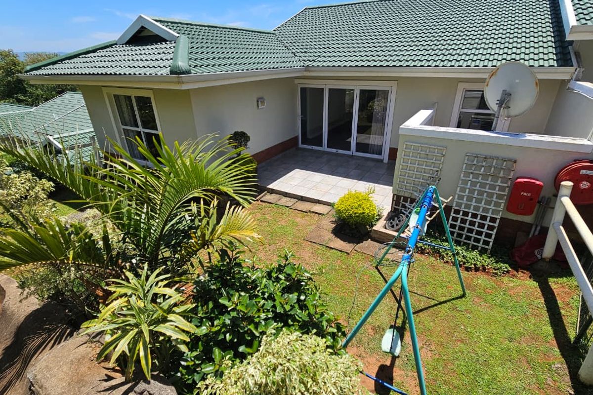 A rear view of the townhouse featuring a tiled patio area, landscaped garden, and green tiled roof.