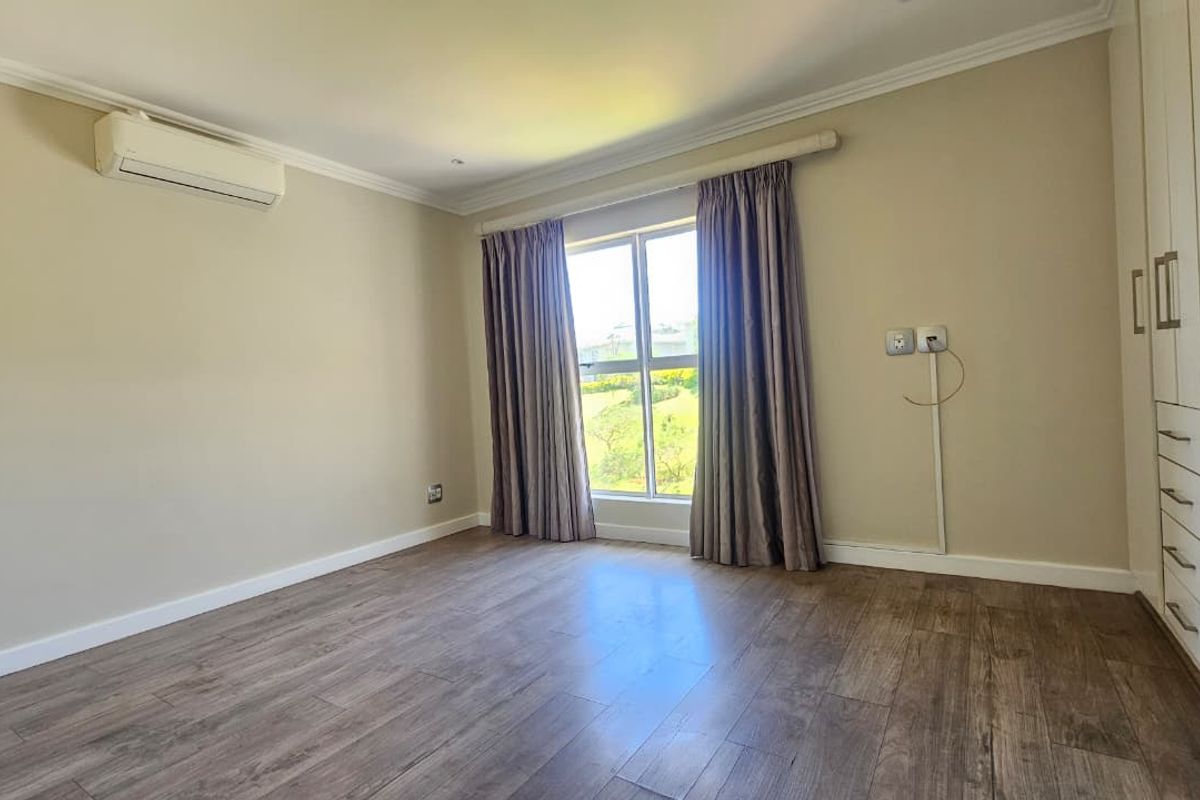 A bright bedroom featuring wood-look flooring, built-in cabinetry, and a wall-mounted air conditioning unit.