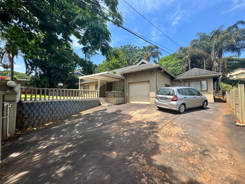 Front exterior view of a single-story house featuring a tiled roof, attached garage, concrete driveway, and a raised patio area with balustrades.