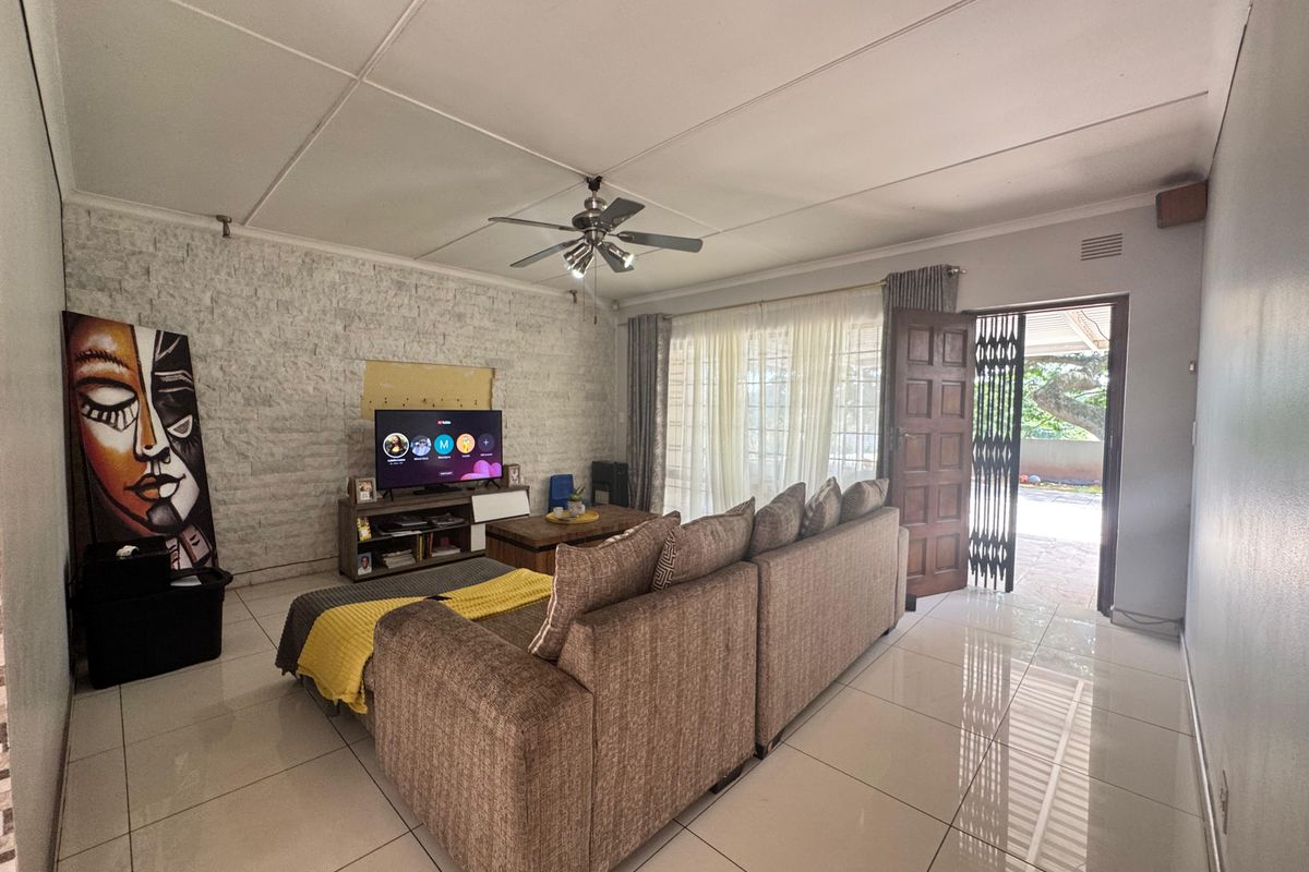 Spacious living room featuring tiled flooring, a stone accent wall, and a ceiling fan, with direct access to the outdoor area through a sliding door.