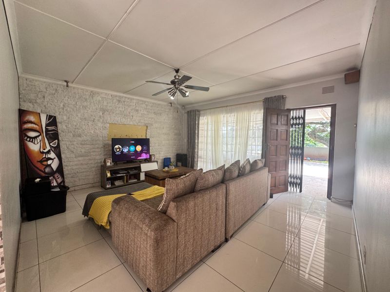 Spacious living room featuring tiled flooring, a stone accent wall, and a ceiling fan, with direct access to the outdoor area through a sliding door.