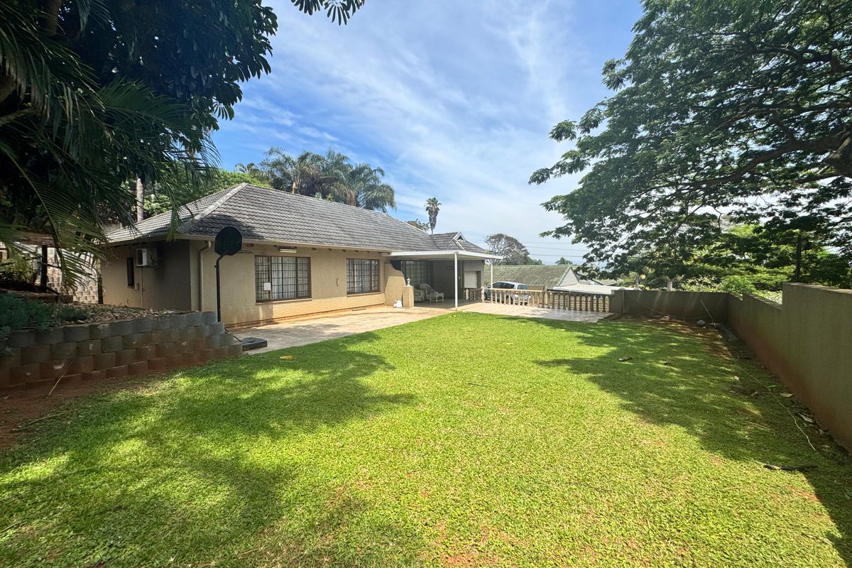 Rear view of the house featuring a spacious lawn, a covered patio area with concrete balustrades, and a tiled roof.