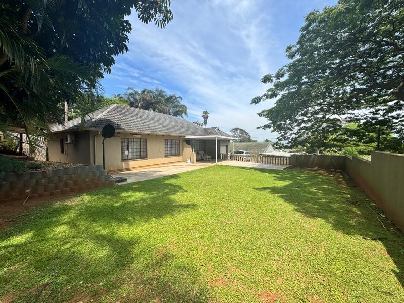 Rear view of the house featuring a spacious lawn, a covered patio area with concrete balustrades, and a tiled roof.