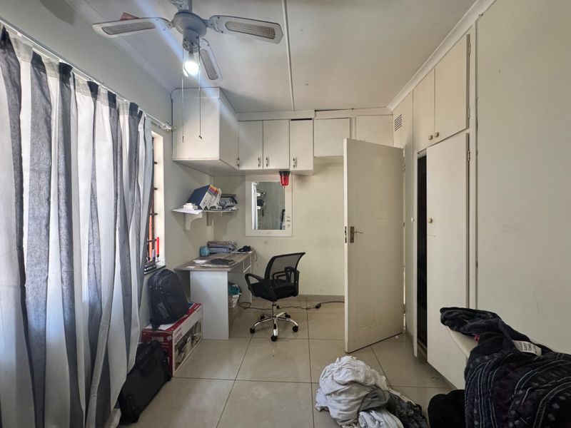 A bedroom featuring built-in cupboards, a built-in desk, and a ceiling fan, finished with tiled flooring.
