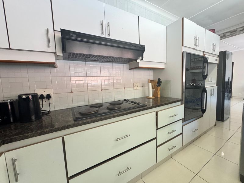 Functional kitchen featuring white cabinetry, dark laminate countertops, built-in double oven, electric hob, and tiled backsplash with neutral floor tiles.