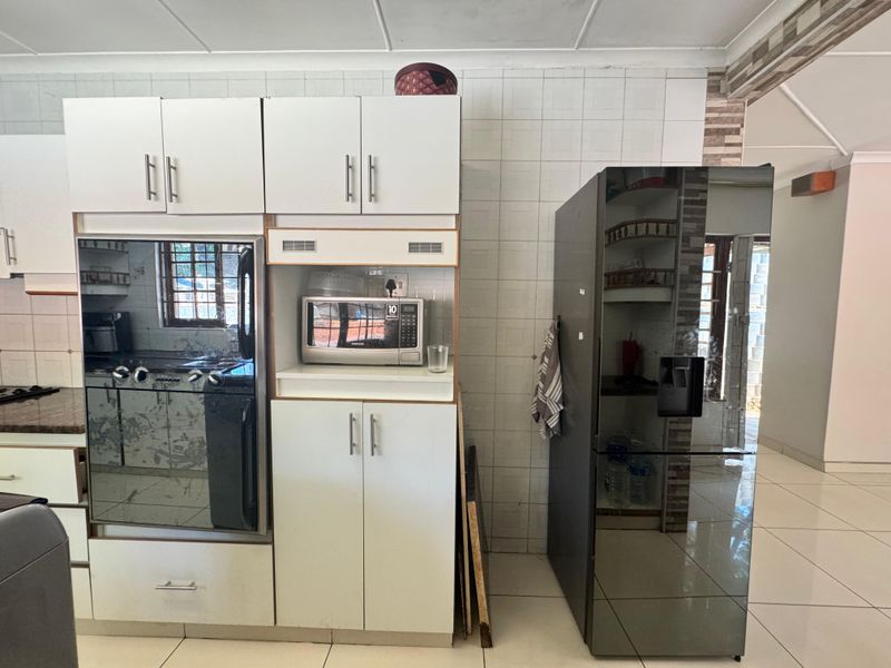 A functional kitchen area featuring built-in cabinetry, an integrated oven, and a microwave, finished with tiled walls and flooring.
