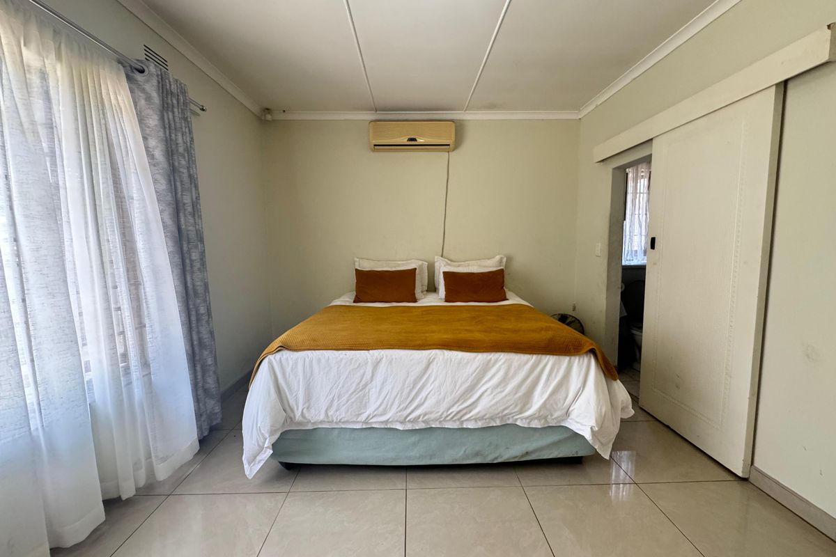 A bedroom featuring tiled flooring, a wall-mounted air conditioning unit, and a sliding door leading to an adjacent space.