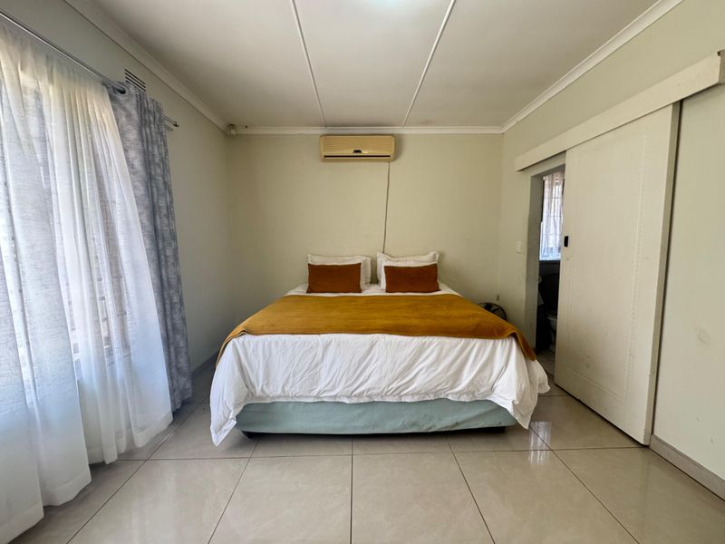A bedroom featuring tiled flooring, a wall-mounted air conditioning unit, and a sliding door leading to an adjacent space.