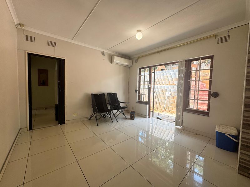 A bright, tiled living room featuring an air conditioning unit and direct access to an outdoor area through a sliding glass door.