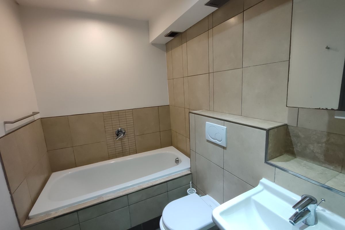 A functional bathroom featuring a built-in bathtub, wall-mounted toilet with concealed cistern, and a modern basin with chrome fixtures.