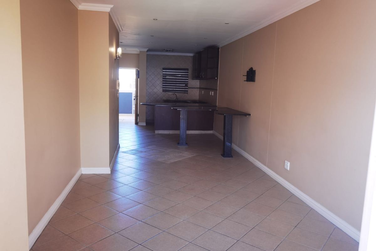 An open-plan living and kitchen area featuring tiled flooring, built-in cabinetry, and a breakfast bar, offering a functional and versatile living space.