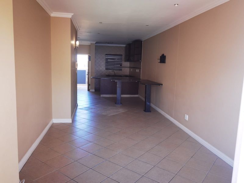 An open-plan living and kitchen area featuring tiled flooring, built-in cabinetry, and a breakfast bar, offering a functional and versatile living space.
