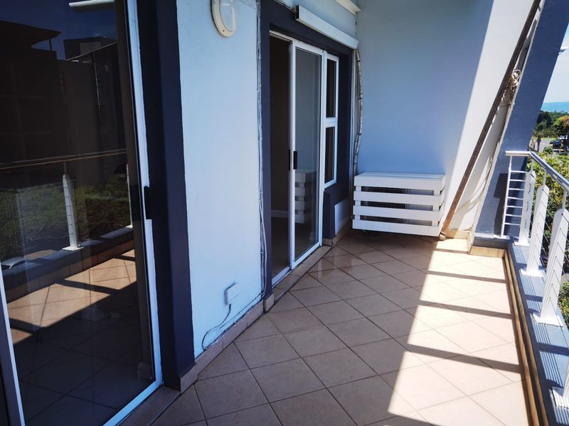 A spacious balcony featuring tiled flooring, metal balustrades, and sliding glass door access, offering a functional outdoor living space.