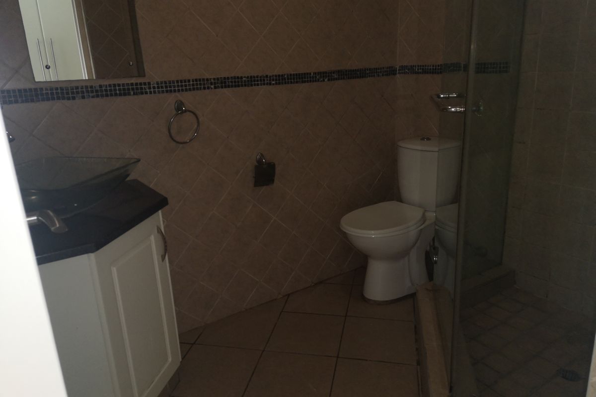 A functional bathroom featuring a vanity with a vessel sink, a toilet, and a glass-enclosed shower with tiled finishes throughout.