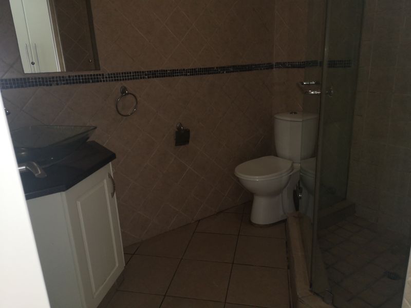 A functional bathroom featuring a vanity with a vessel sink, a toilet, and a glass-enclosed shower with tiled finishes throughout.