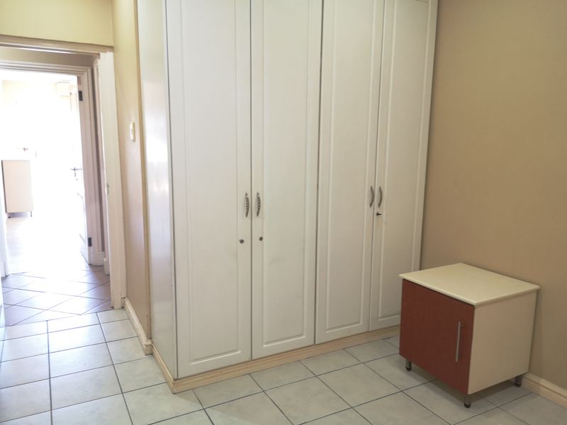 A bedroom featuring built-in white cupboards and tiled flooring, with a view leading into an adjacent hallway.