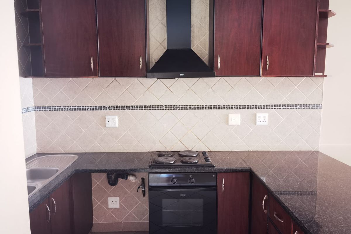 A functional kitchen featuring dark wood cabinetry, granite countertops, a built-in oven with hob, and a tiled backsplash.