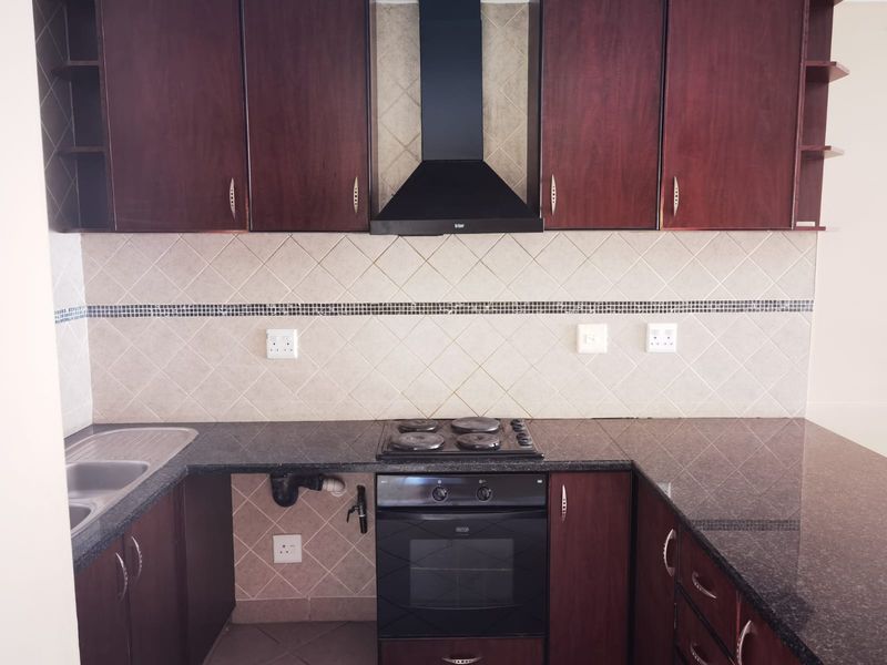 A functional kitchen featuring dark wood cabinetry, granite countertops, a built-in oven with hob, and a tiled backsplash.