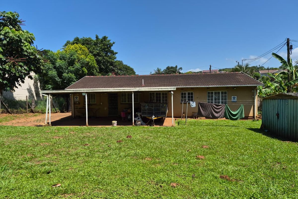 Rear view of the house featuring a covered patio area, tiled roof, and a spacious garden with a small storage shed.
