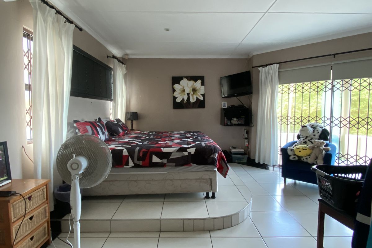 Spacious bedroom featuring a raised tiled platform for the bed area, large windows with security gates, and neutral wall finishes.