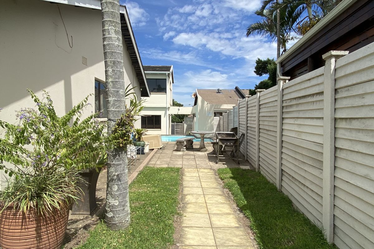 A side garden pathway leading to a paved patio area with a swimming pool in the background.