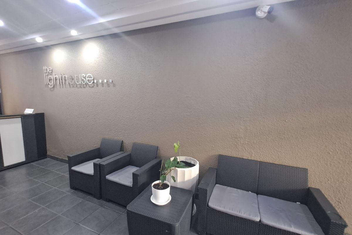 A modern apartment building entrance lobby featuring tiled flooring, recessed ceiling lighting, and a textured feature wall with building signage.