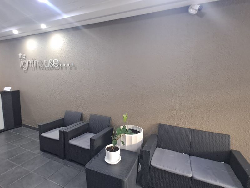 A modern apartment building entrance lobby featuring tiled flooring, recessed ceiling lighting, and a textured feature wall with building signage.