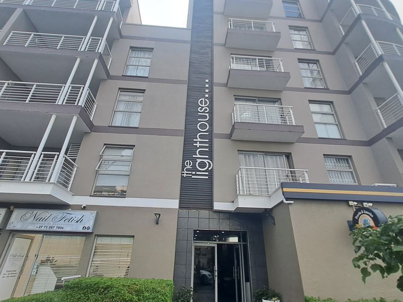 Exterior view of The Lighthouse apartment building, featuring a multi-story facade with private balconies and ground-floor commercial retail spaces.