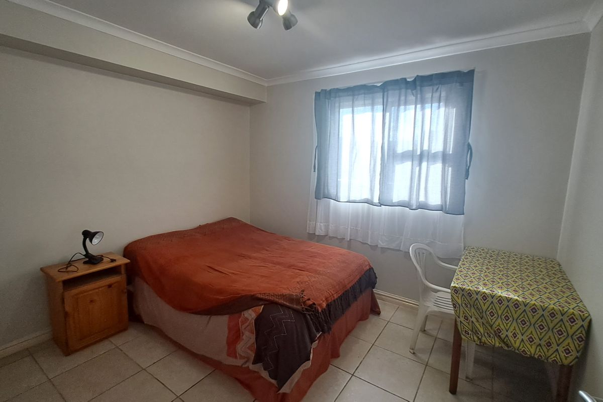 A functional bedroom featuring tiled flooring, neutral wall finishes, and a window with fitted curtain tracks.