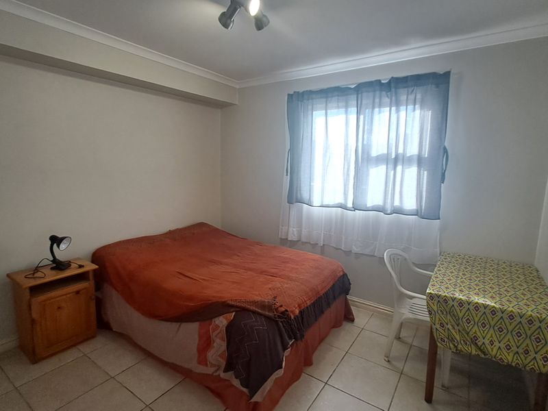 A functional bedroom featuring tiled flooring, neutral wall finishes, and a window with fitted curtain tracks.