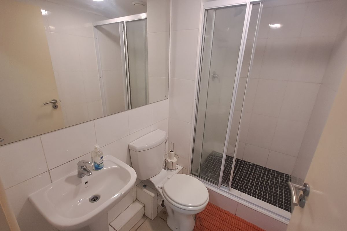 A functional bathroom featuring a pedestal sink, a white toilet, and a glass-enclosed shower with dark tiled flooring.