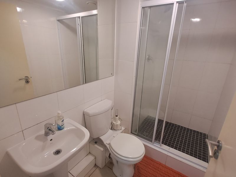 A functional bathroom featuring a pedestal sink, a white toilet, and a glass-enclosed shower with dark tiled flooring.