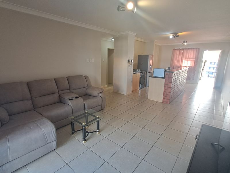 Open-plan living and kitchen area featuring tiled flooring, a brick-faced breakfast bar, and direct access to an outdoor space.