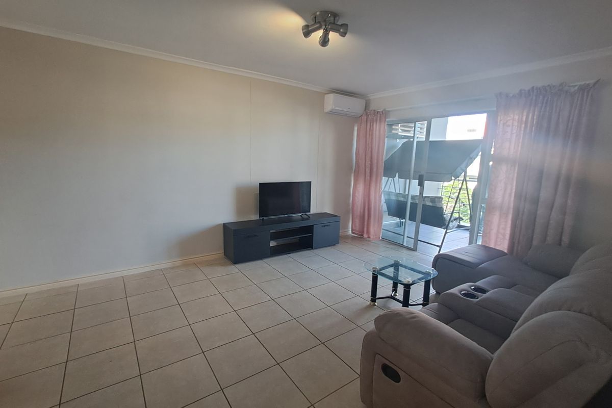 Spacious living area featuring tiled flooring, a wall-mounted air conditioning unit, and sliding glass doors providing access to an outdoor patio.