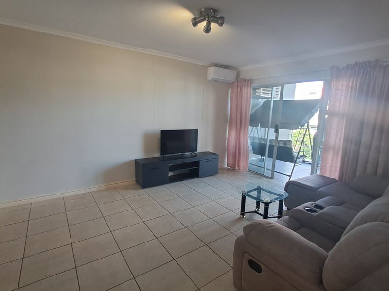 Spacious living area featuring tiled flooring, a wall-mounted air conditioning unit, and sliding glass doors providing access to an outdoor patio.