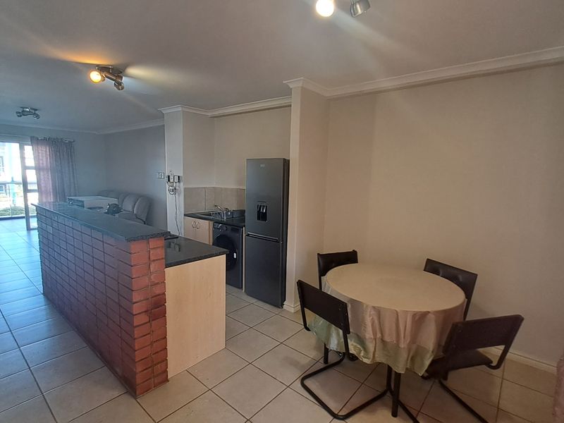 Open plan living and kitchen area featuring a brick-faced breakfast bar, tiled flooring, and direct access to a balcony.