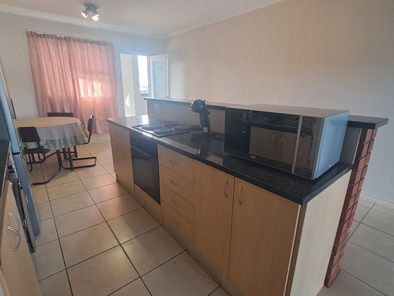 Open plan kitchen featuring a breakfast bar, built-in oven, hob, and tiled flooring, seamlessly connecting to the adjacent dining area.