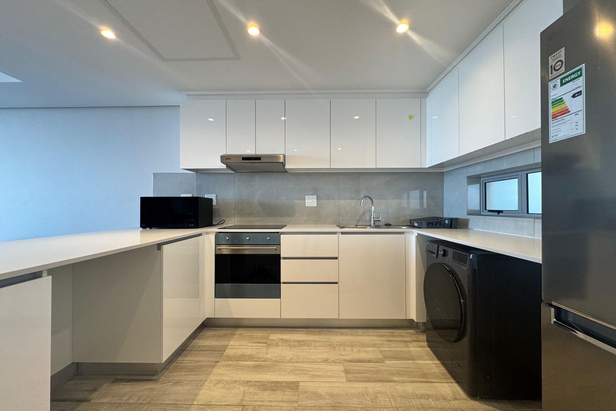 Modern kitchen featuring sleek white cabinetry, stone countertops, integrated oven, hob, extractor fan, and a dedicated space for laundry appliances.
