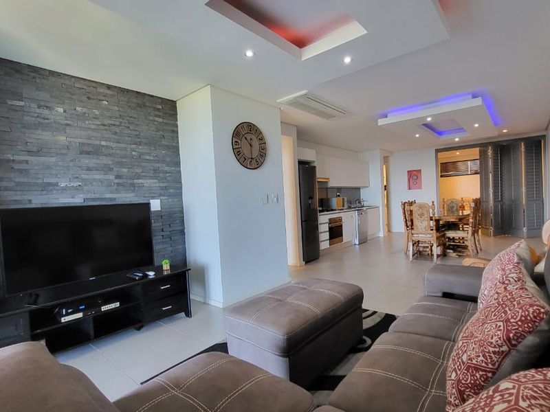 Spacious open-plan living and dining area featuring a modern stacked stone feature wall, recessed ceiling lighting, and a sleek, well-appointed kitchen.