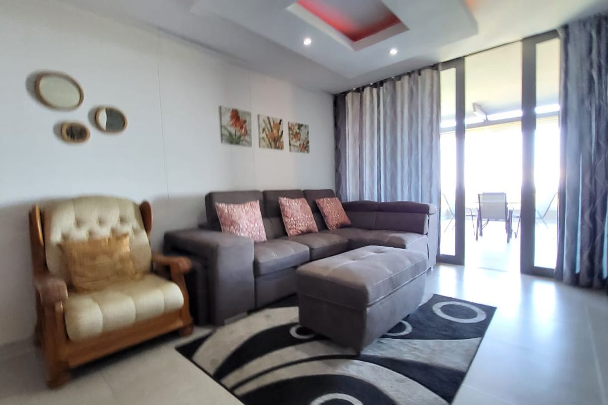 A well-lit living room featuring tiled flooring, recessed ceiling lighting, and large sliding glass doors providing access to an outdoor balcony area.