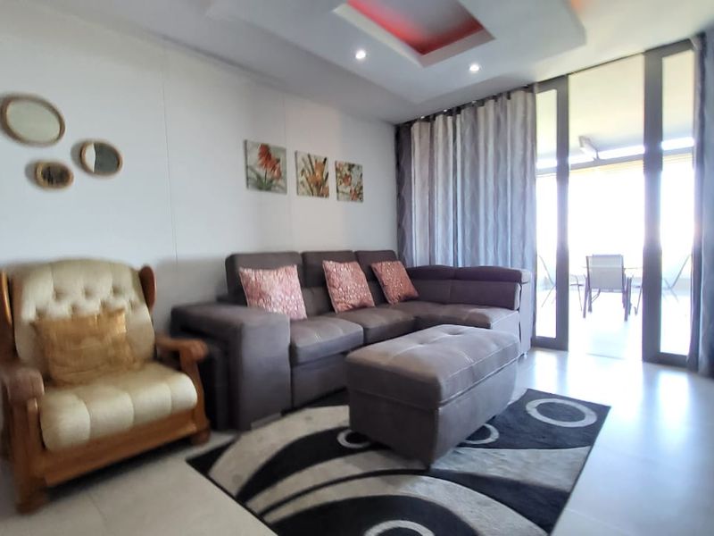 A well-lit living room featuring tiled flooring, recessed ceiling lighting, and large sliding glass doors providing access to an outdoor balcony area.