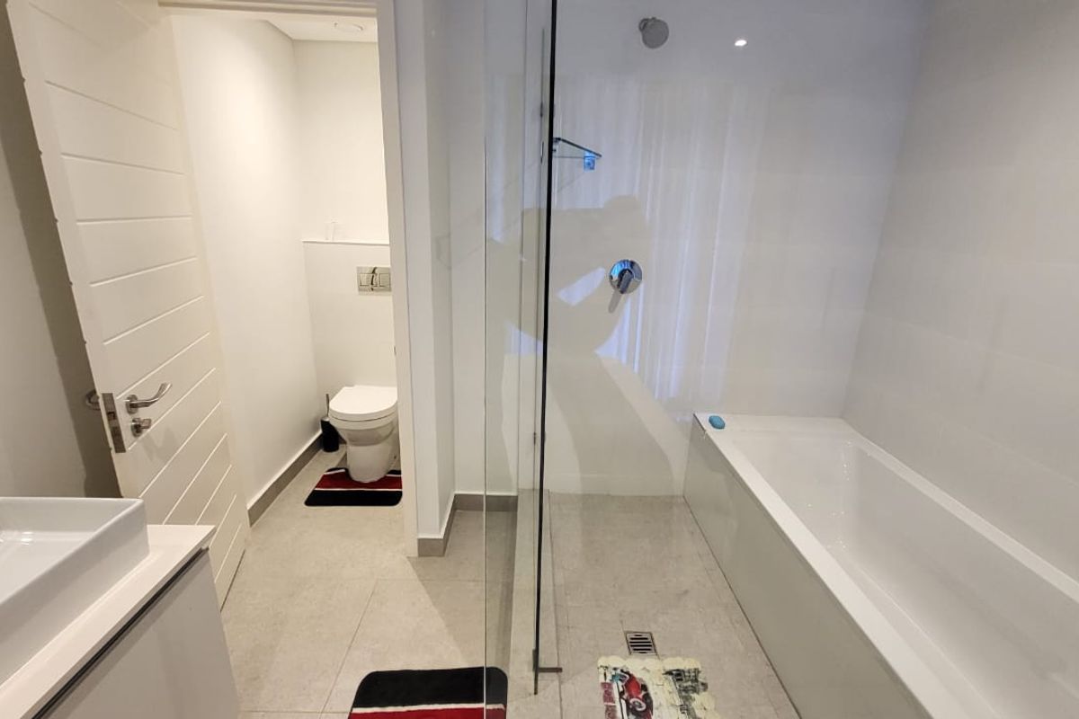 Modern bathroom featuring a built-in bathtub, glass shower enclosure, wall-mounted toilet, and a sleek vanity with a basin.