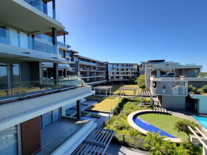 Elevated view of a modern apartment complex featuring landscaped gardens, a swimming pool, and private balconies with glass balustrades.