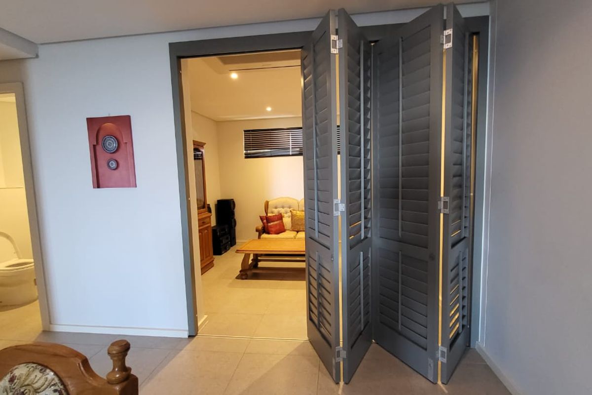 Bedroom featuring grey bi-fold shutters leading to an adjacent living area, with tiled flooring and recessed ceiling lighting.