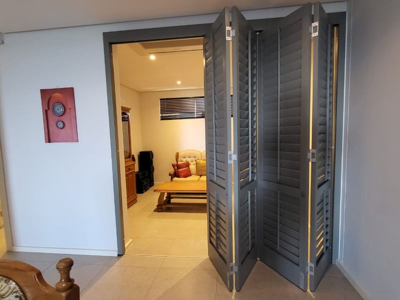 Bedroom featuring grey bi-fold shutters leading to an adjacent living area, with tiled flooring and recessed ceiling lighting.