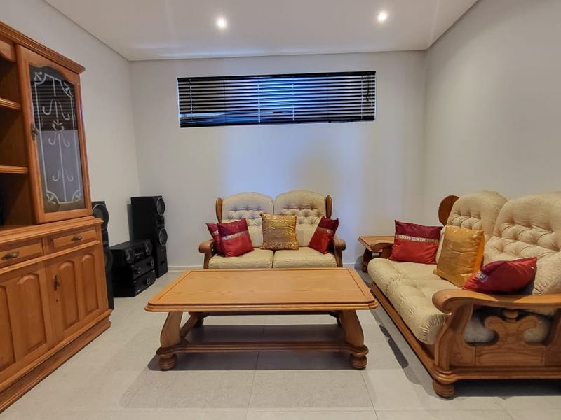 A living room featuring neutral tiled flooring, recessed ceiling lighting, and a horizontal window with fitted venetian blinds.