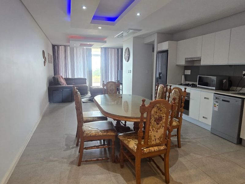 Open-plan living and dining area featuring a modern kitchen with built-in cabinetry, integrated appliances, and recessed ceiling lighting leading to a balcony.