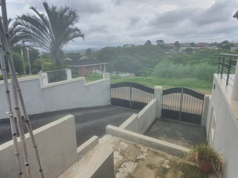 Front exterior view featuring a paved driveway, secure wrought iron gates, concrete boundary walls, and a tiled balcony with metal railings.