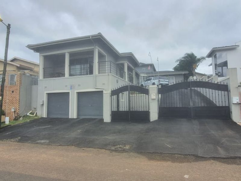 Front elevation of a multi-level house featuring a double garage with roller doors, a paved driveway, and a balcony with metal balustrades.
