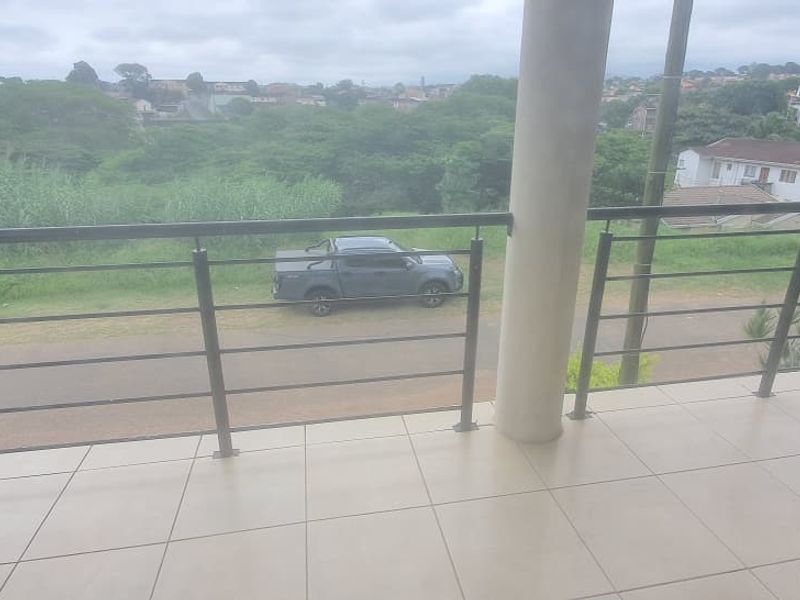 A covered balcony featuring tiled flooring, concrete support columns, and a metal balustrade overlooking the surrounding neighborhood.